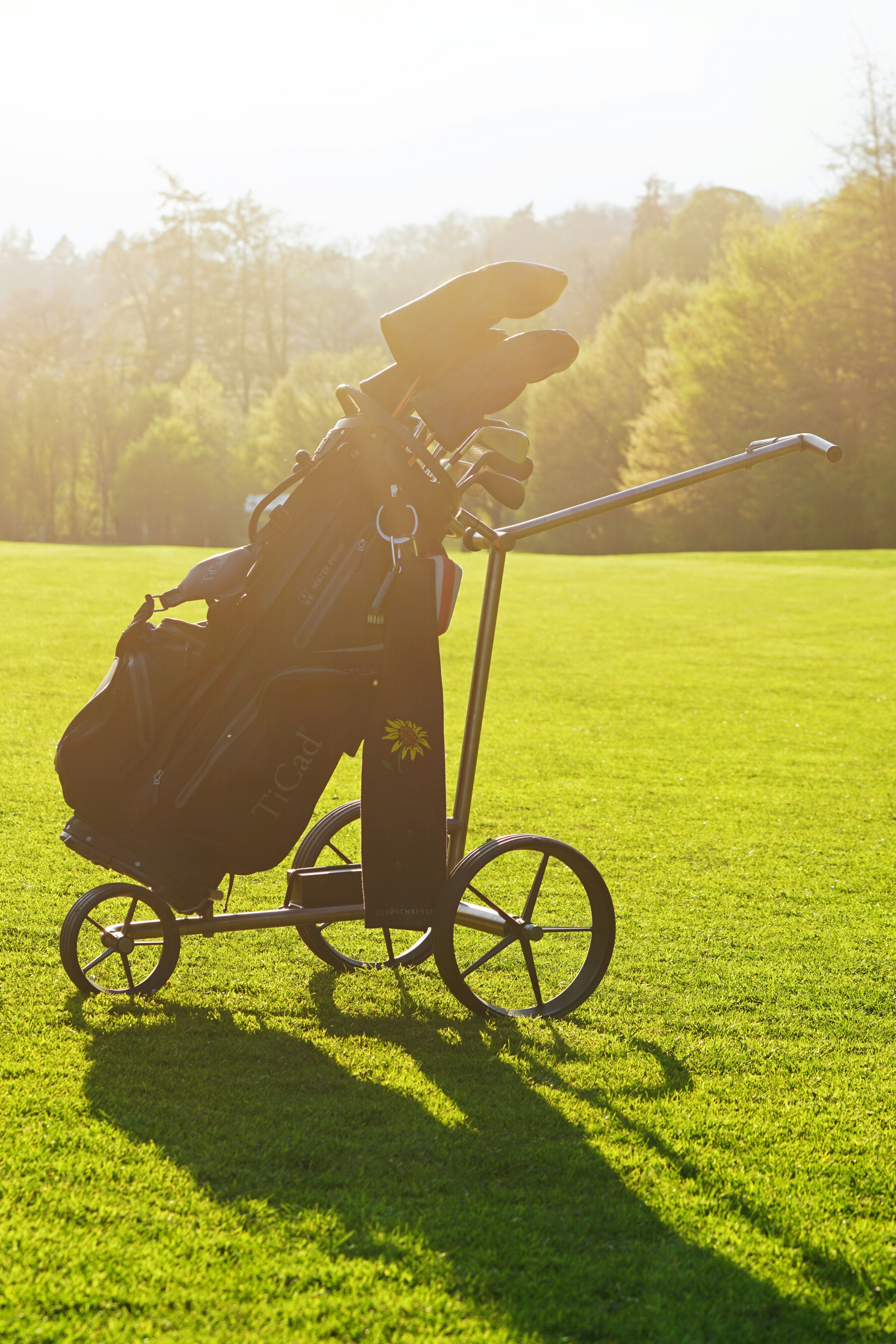 A golf course showing a golfer walking with a push cart on a beautiful sunny day