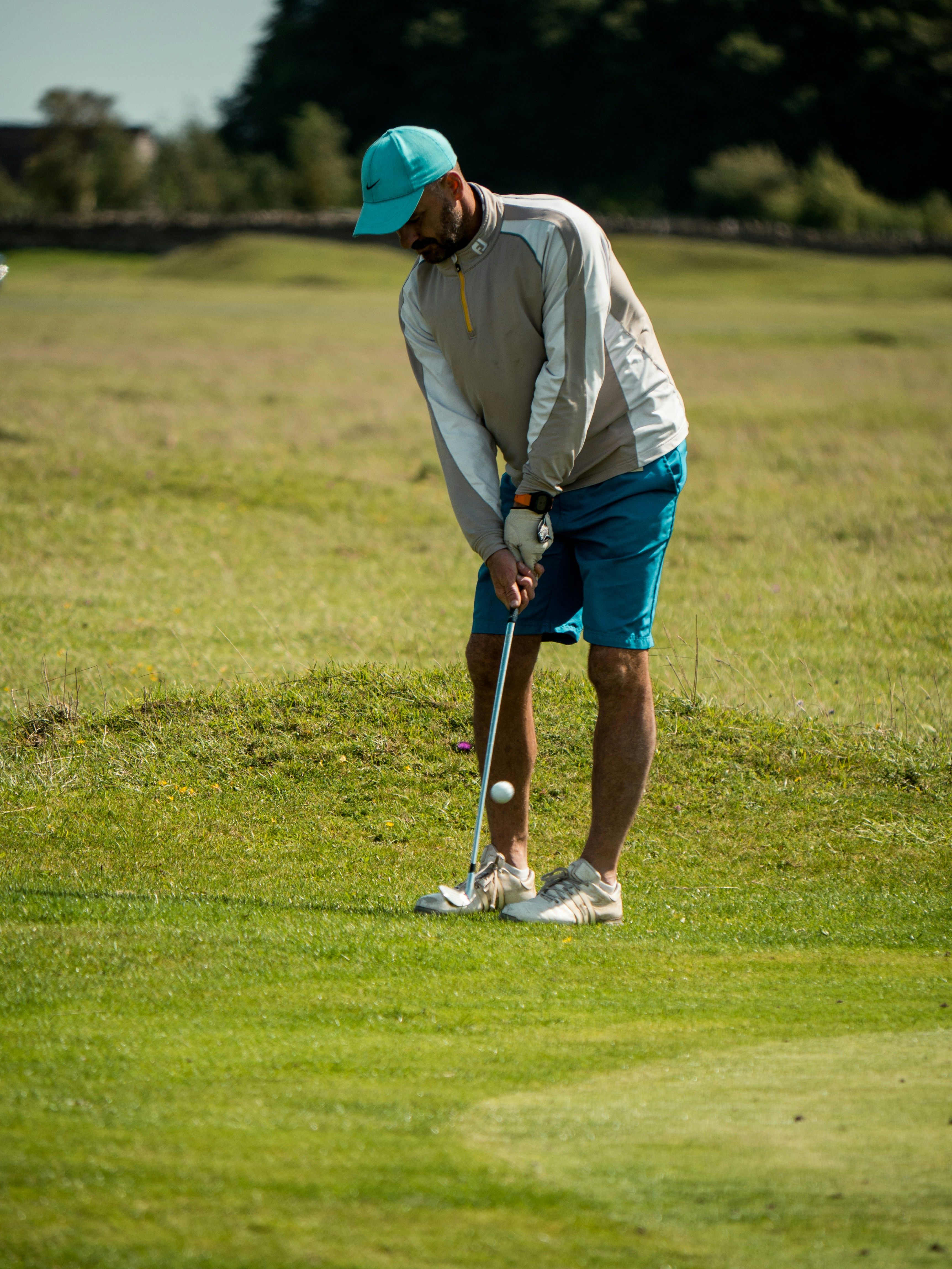 A left-handed golfer in red cap swinging a golf club on a green course